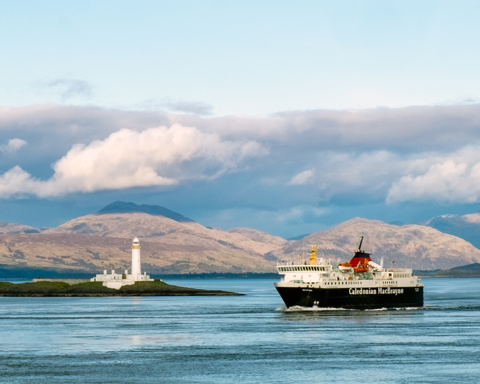 Ferry sailing near lighthouse and mountains